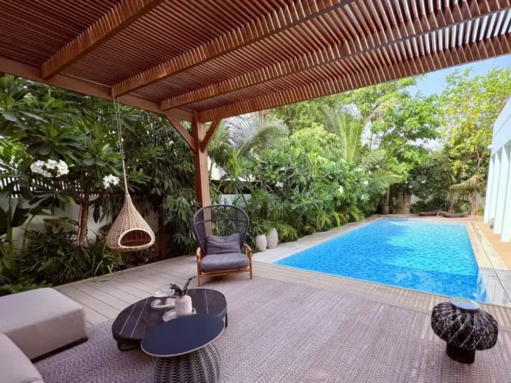 Timber pergola over outdoor seating, a hanging chair and planting at a villa